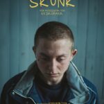 Ein Junge mit gesenktem Blick vor einem türkisen Hintergrund mit Overall - Skunk