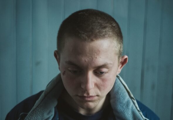 Ein Junge mit gesenktem Blick vor einem türkisen Hintergrund mit Overall - Skunk